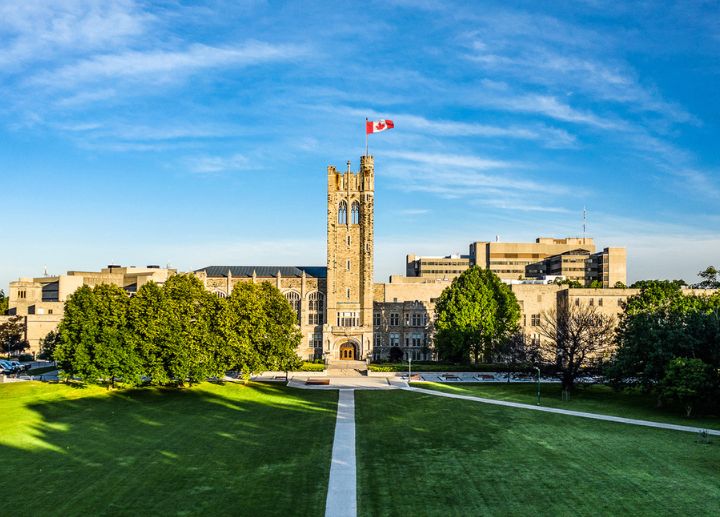 Front view of University College building at Western University and a large green lawn under a blue sky